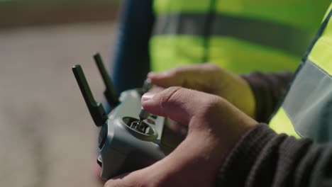 persona que controla un dron al aire libre utilizando un control remoto, primer plano de las manos en una chaqueta de alta visibilidad