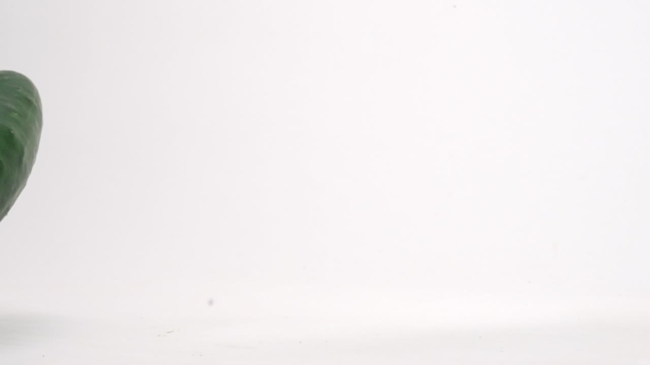 cerca de pepinos enteros verdes frescos rebotando en la parte superior de la mesa blanca en cámara lenta