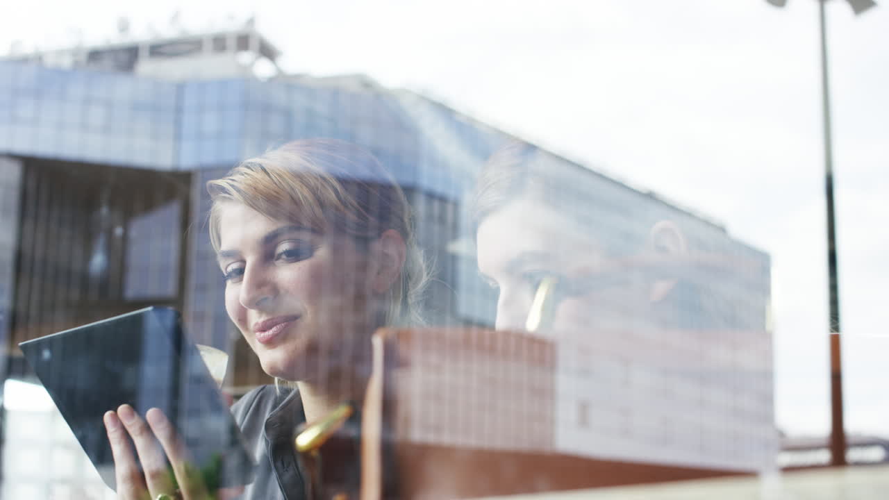 두 여자 친구가 카페에서 디지털 태블릿을 사용하여 커피를 나누고 있습니다.