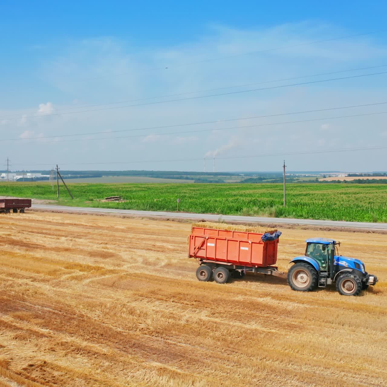 Agricultural machine moving by the cut wheat field. Tractor downloaded with hay bales rides by the plantation. High angle view