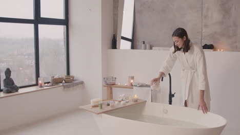 Mujer-En-Bata-De-Baño-Vierte-Sales-De-Baño-En-La-Bañera-Y-Luego-Toca-El-Agua