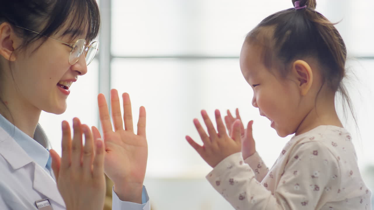 Asian Pediatrician Playing Hand Clapping Game with Toddler Girl