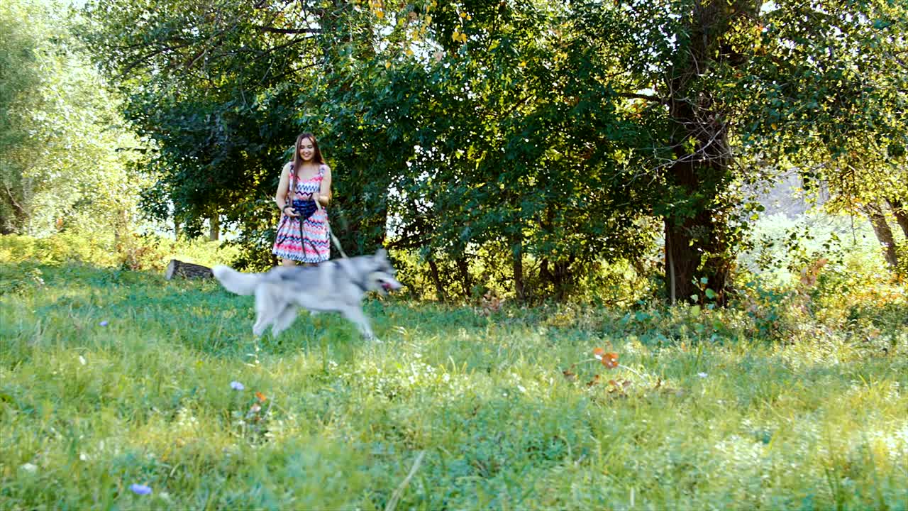 una mujer joven está jugando en el bosque con un perro husky.
