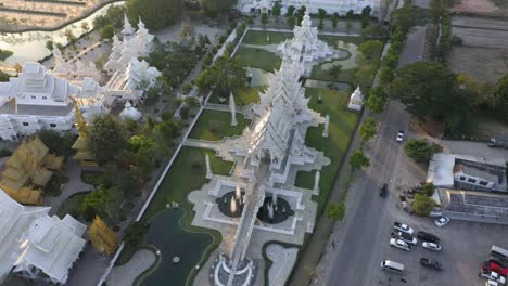 Luftdrohne-Des-Riesigen-Buddhistischen-Weißen-Tempels-Wat-Rong-Khun-Und-Des-Goldenen-Tempels-Mit-Bergen-Und-Landschaft-In-Chiang-Rai,-Thailand