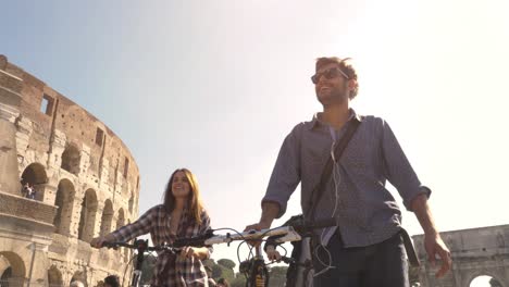 three young friends tourists walking with bikes and backpack at colosseum in rome on sunny day slow motion camera steadycam ground shot