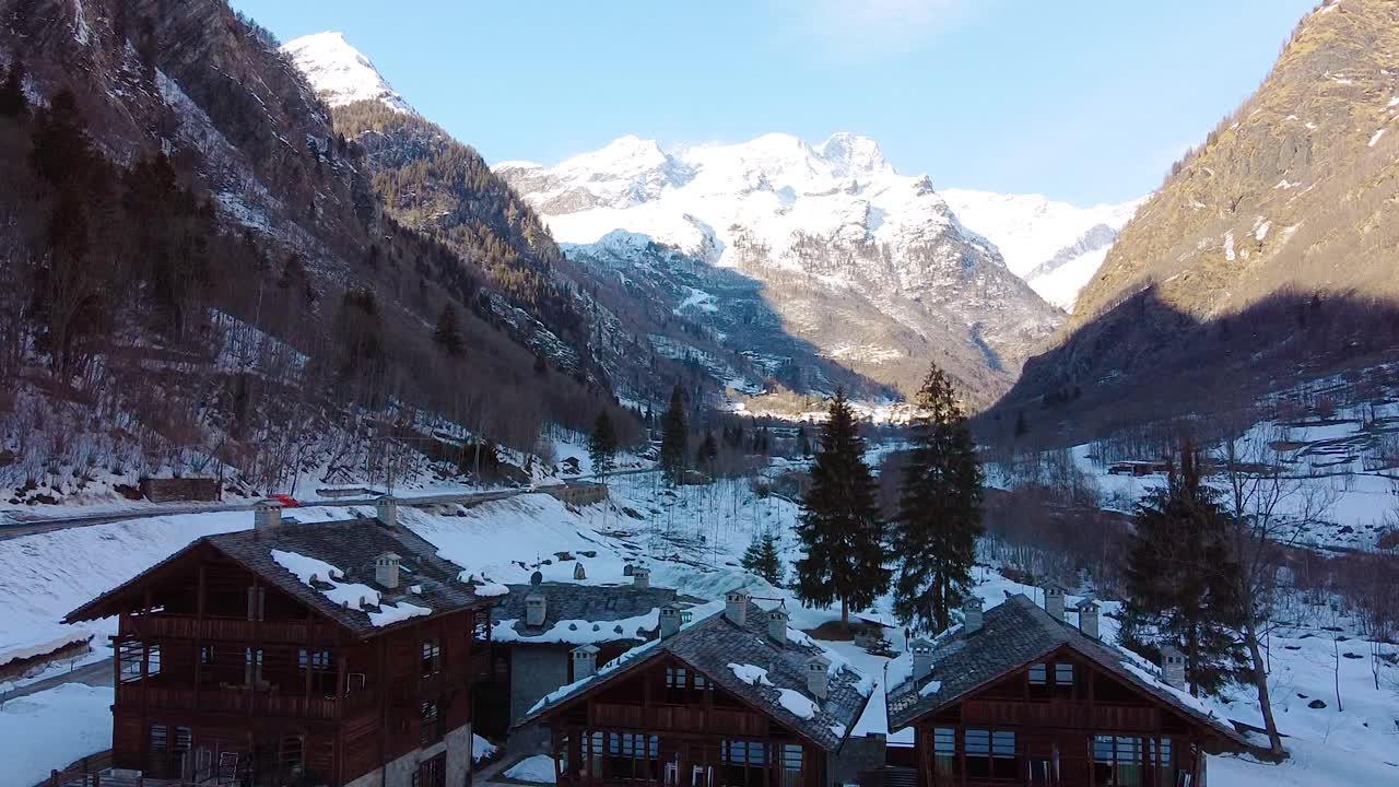 Ripresa cinematografica con drone durante l'inverno che mostra baite in legno e montagne sullo sfondo con molta neve