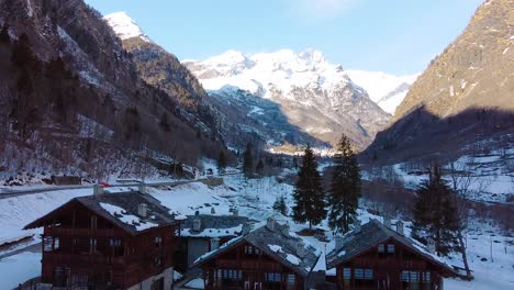 Cinematic-drone-shot-during-winter-showing-wooden-cabins-and-mountains-in-the-back-with-a-lot-of-snow