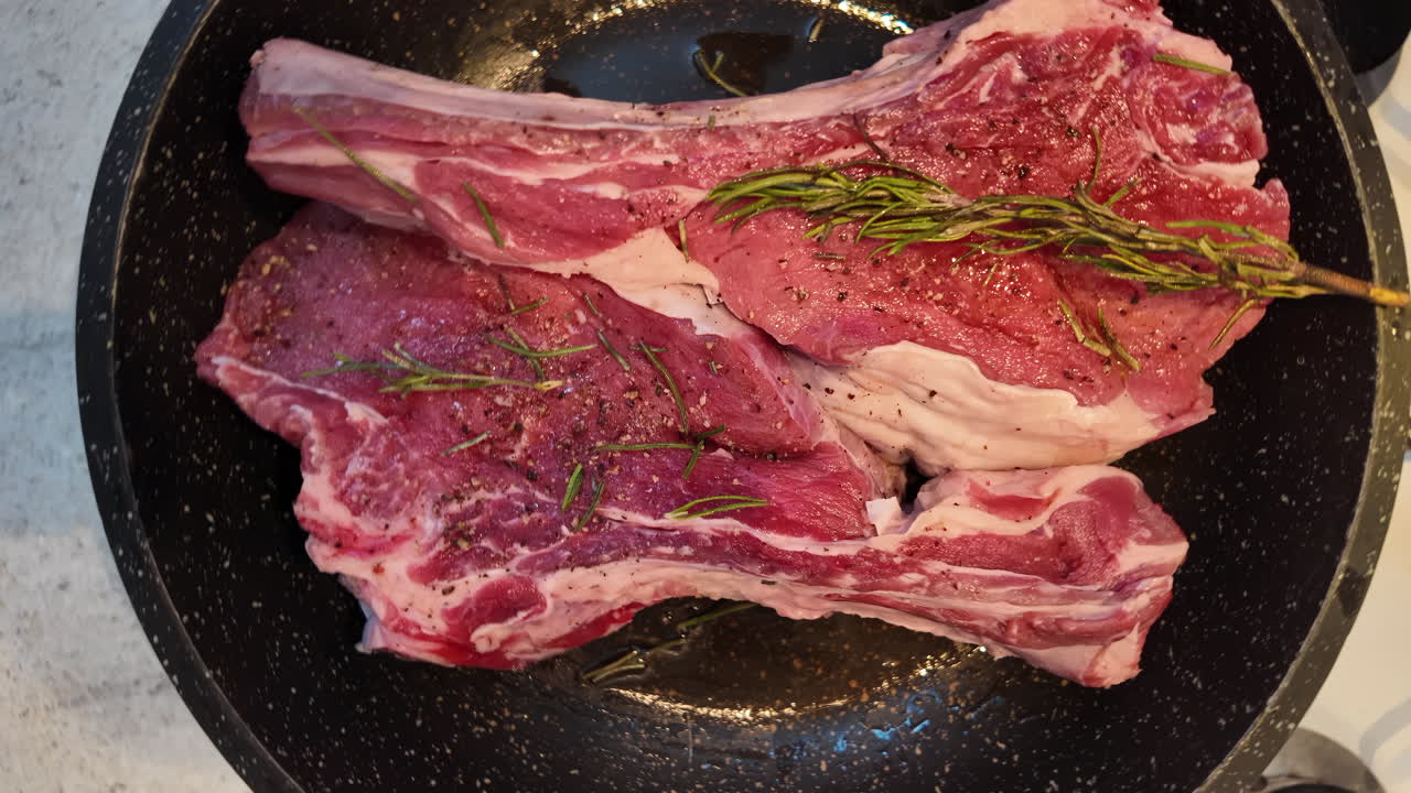 Big red beef stake on a black pan with rosemary ready for cooking, black pepper on top