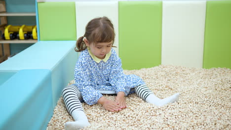 niña pequeña jugando en piscina seca, rastrillando cubos de madera hinoki suave haciendo montones o pilas en el centro de entretenimiento infantil, desarrollo de sensores táctiles