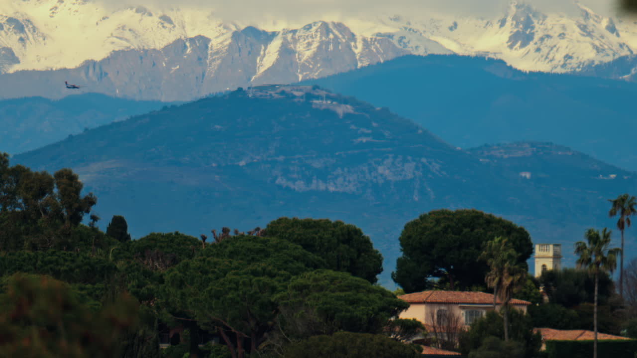 Distant view of orange villas surrounded by green trees with the mountains on the background on a cloudy day