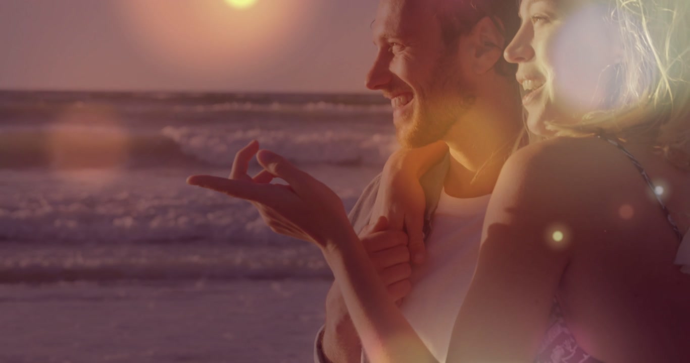 Man gesturing to horizon, woman leaning touching chest at beach sunset, bokeh drifting, travel ad