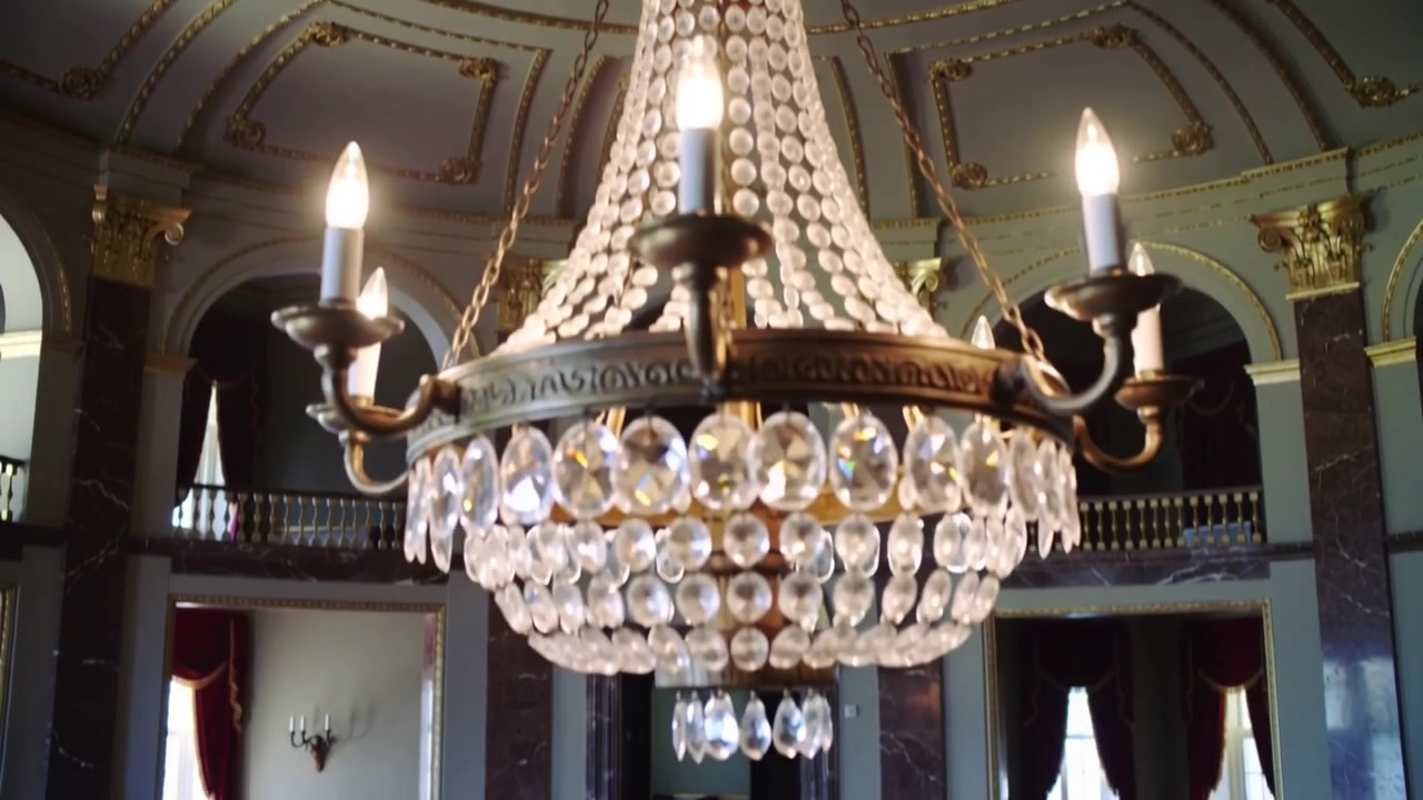 Telecamera che si inclina rivelando un lampadario di cristallo in una sala da ballo, mostrando dettagli dei cristalli e la grandezza della sala
