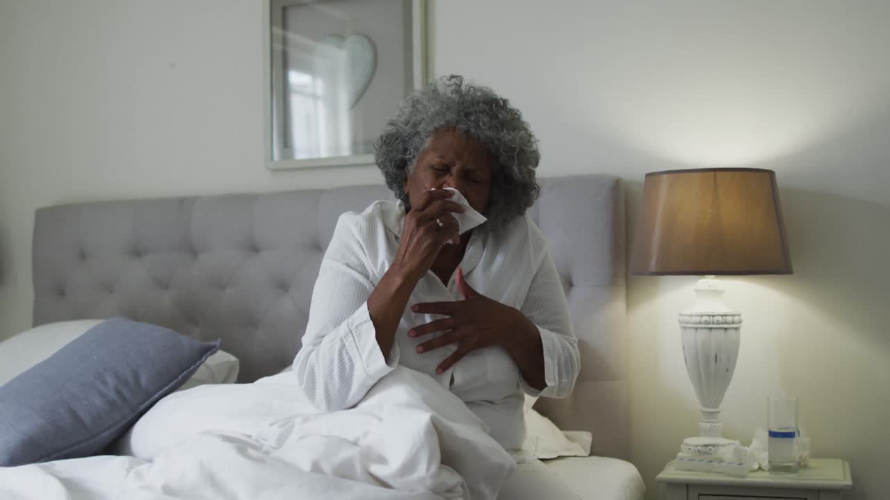 Sick senior african american woman coughing while sitting on the bed at home