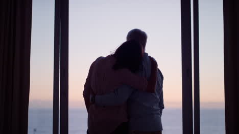 silhouette-happy-old-couple-hugging-in-hotel-room-looking-out-window-at-sunset-enjoying-successful-retirement-lifestyle-on-vacation-sharing-romantic-connection