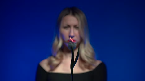 out of focus young beautiful blonde woman with luscious red lips holding a burning white tulip flower on a vivid dark blue background - 4k