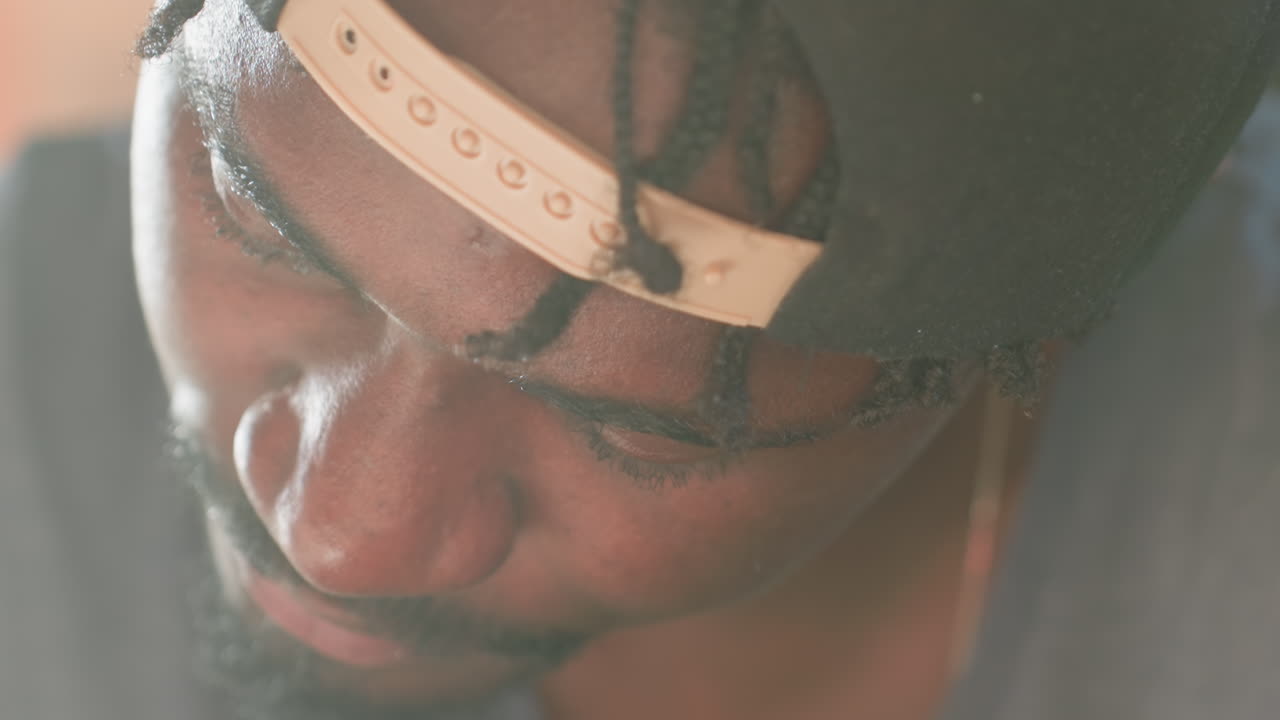 Intensieve close-up van een geconcentreerde donkere man met een focus op zijn taak, ogen neergeslagen, stille concentratie, licht op een gezicht met textuur, vage achtergrond, kalme sfeer, bedachtzame uitdrukking die wijst op studie of probleemoplossing