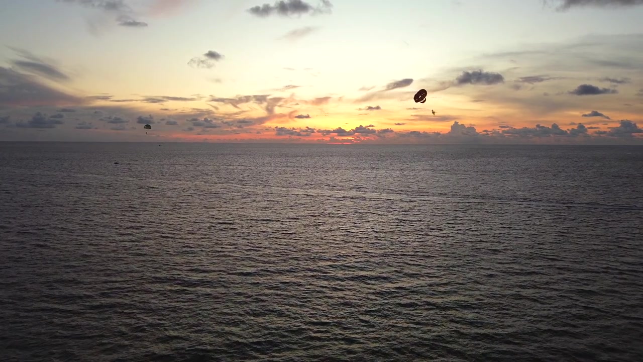 Paragliders svæver over Thailands strand ved solnedgang med farverig himmel og åbent hav nedenfor, luftoptagelse med dolly over åbent vand i havet.