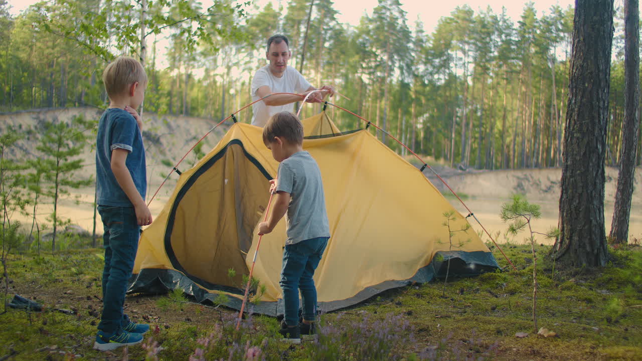 el joven y dos niños juntos montaron una tienda de campaña para pasar la noche durante la campaña. paternidad y una infancia feliz. padre e hijos montaron una tienda de campaña juntos en el bosque