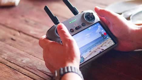 hands operating a drone controller on a wooden table in phuket, with bright lighting and a focus on the screen
