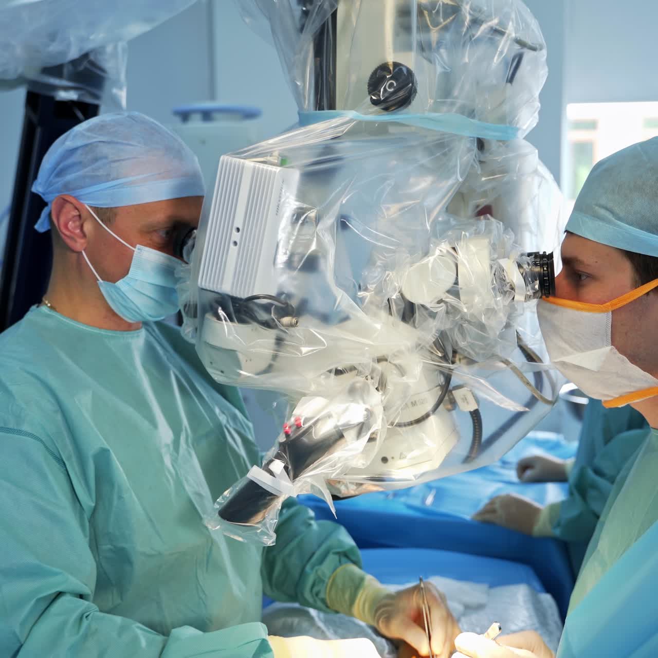 Technological equipment in modern surgery room placed over the operating table. Two surgeons sit and look into binoculars during operation