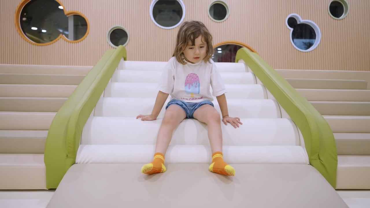 Toddler sliding down indoor bumpy playground slide with excitement and ...
