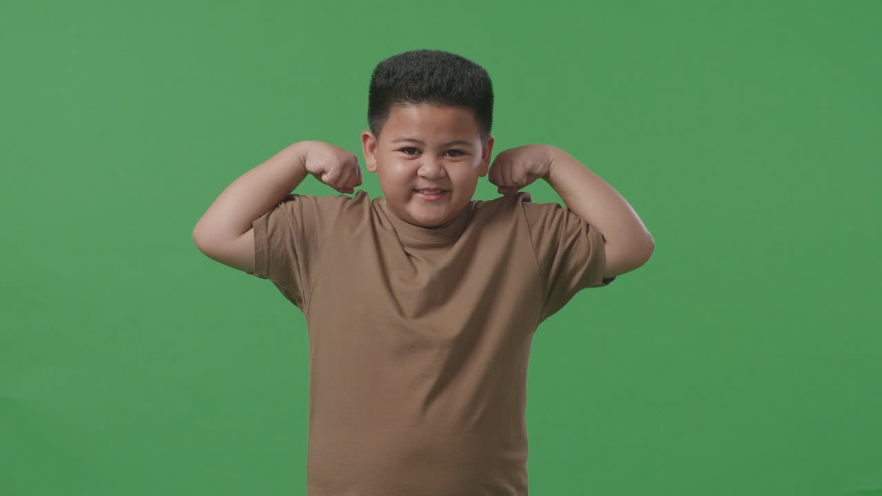 스튜디오의 녹색 스크린 배경에서 아시아 소년이 미소 짓고 근육을 구부린다