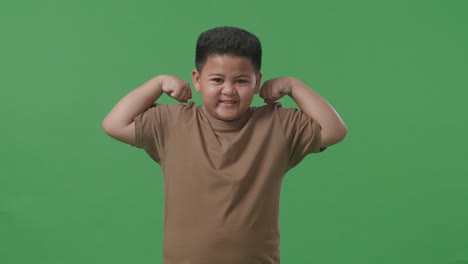 스튜디오의 녹색 스크린 배경에서 아시아 소년이 미소 짓고 근육을 구부린다