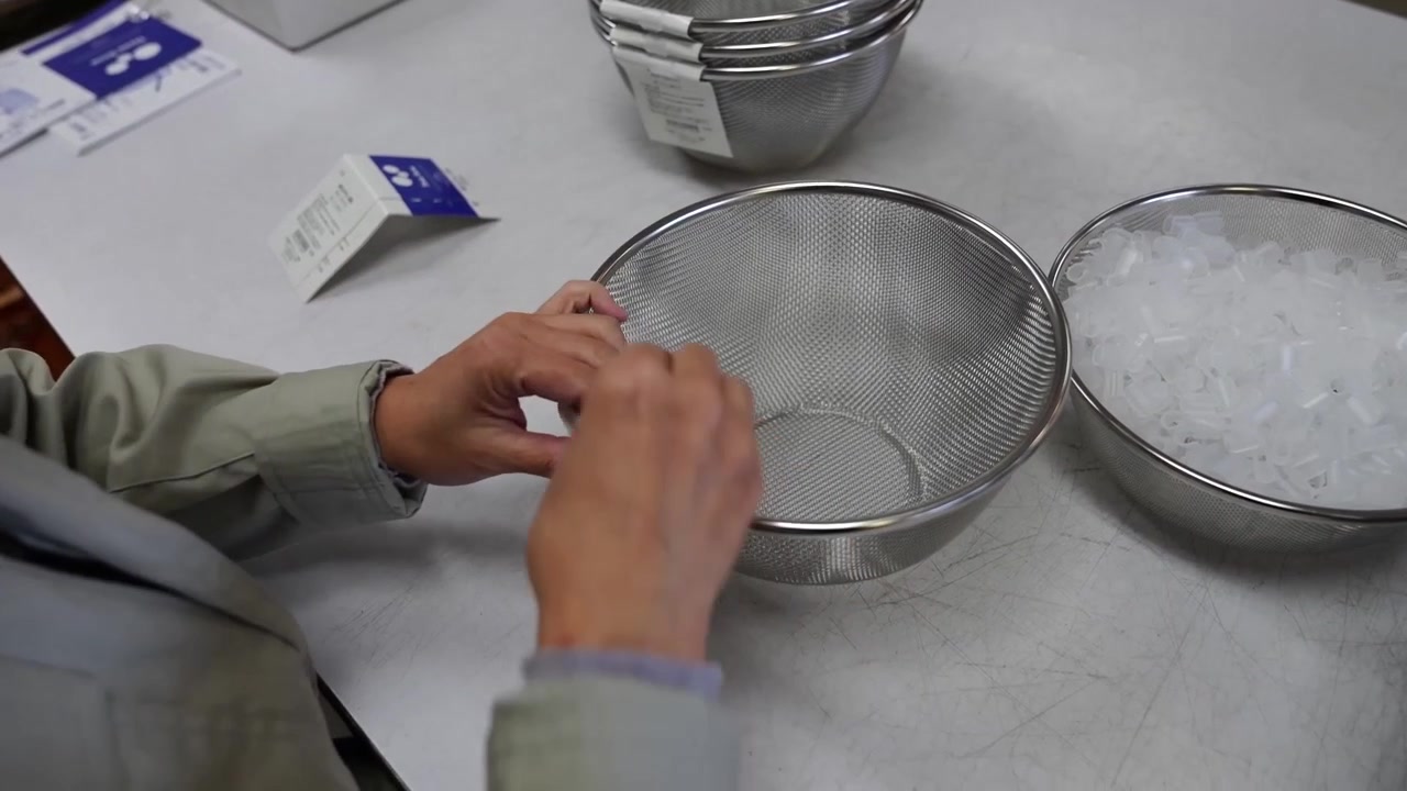 Worker inspecting a wire mesh colander next to a stack of finished bowls on a table