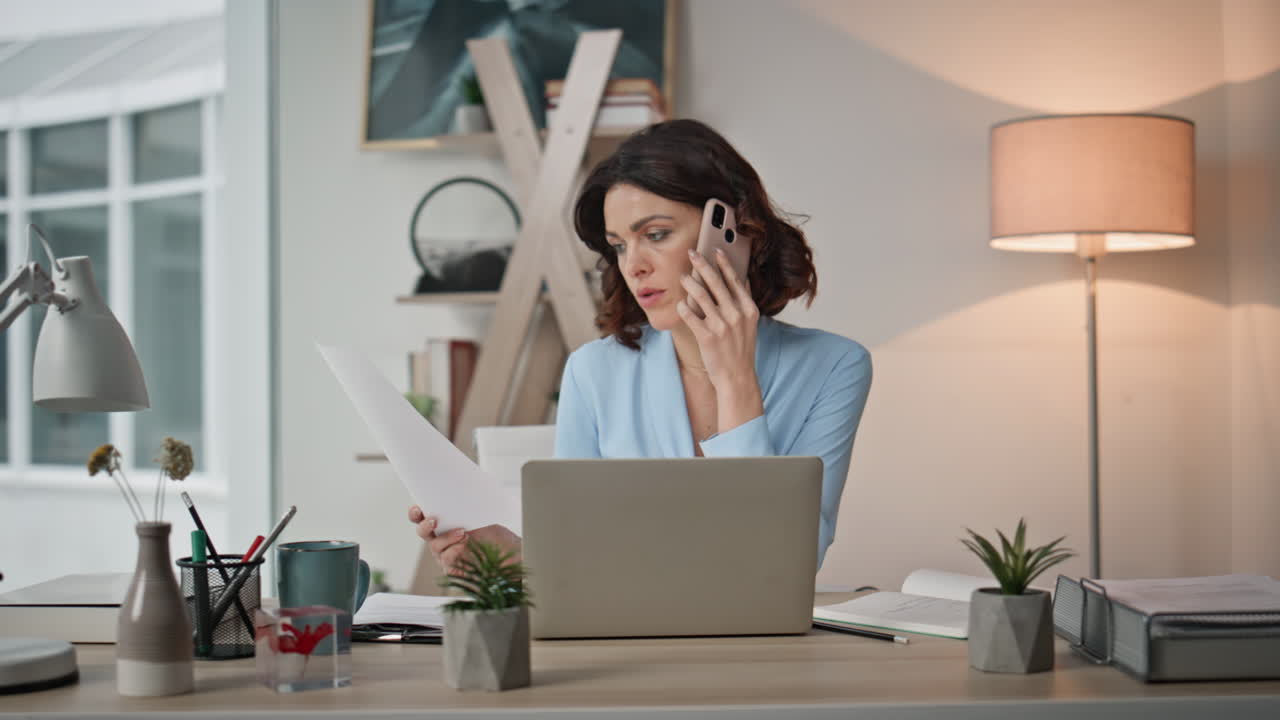 Nærbillede af seriøs kvinde i mobilopkald, der kigger på arbejdsdokumenter på moderne kontor.