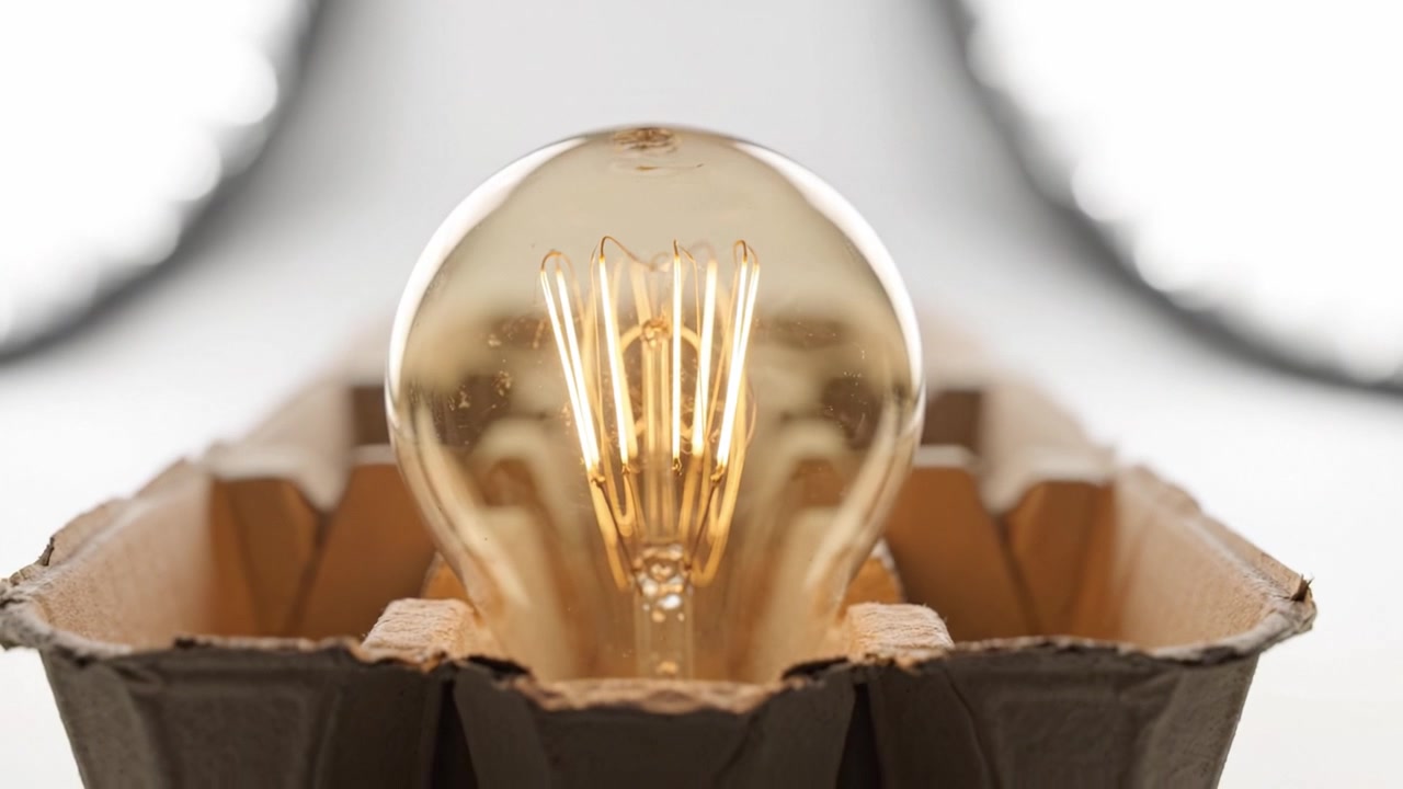 Un primo piano di una lampadina vintage illuminata incastonata in un supporto di cartone ecologico che mostra un bagliore caldo e caratteristiche di design uniche.