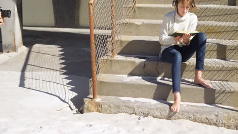 chica escuchando música mientras lee un libro en la playa 4k