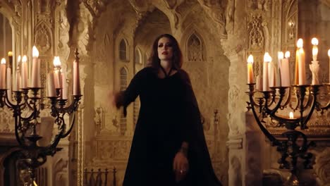mujer con vestido negro y ojos rojos de pie en el castillo gótico con velas