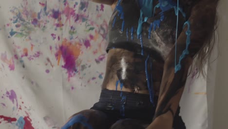 young asian woman in art studio pours blue paint on herself, handheld