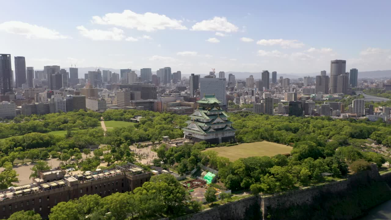 Aerial flying towards historic Osaka Castle with park, moat, skyscraper, and city in Osaka, Japan