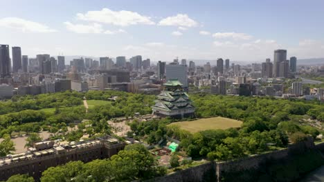 Aerial-flying-towards-historic-Osaka-Castle-with-park,-moat,-skyscraper,-and-city-in-Osaka,-Japan