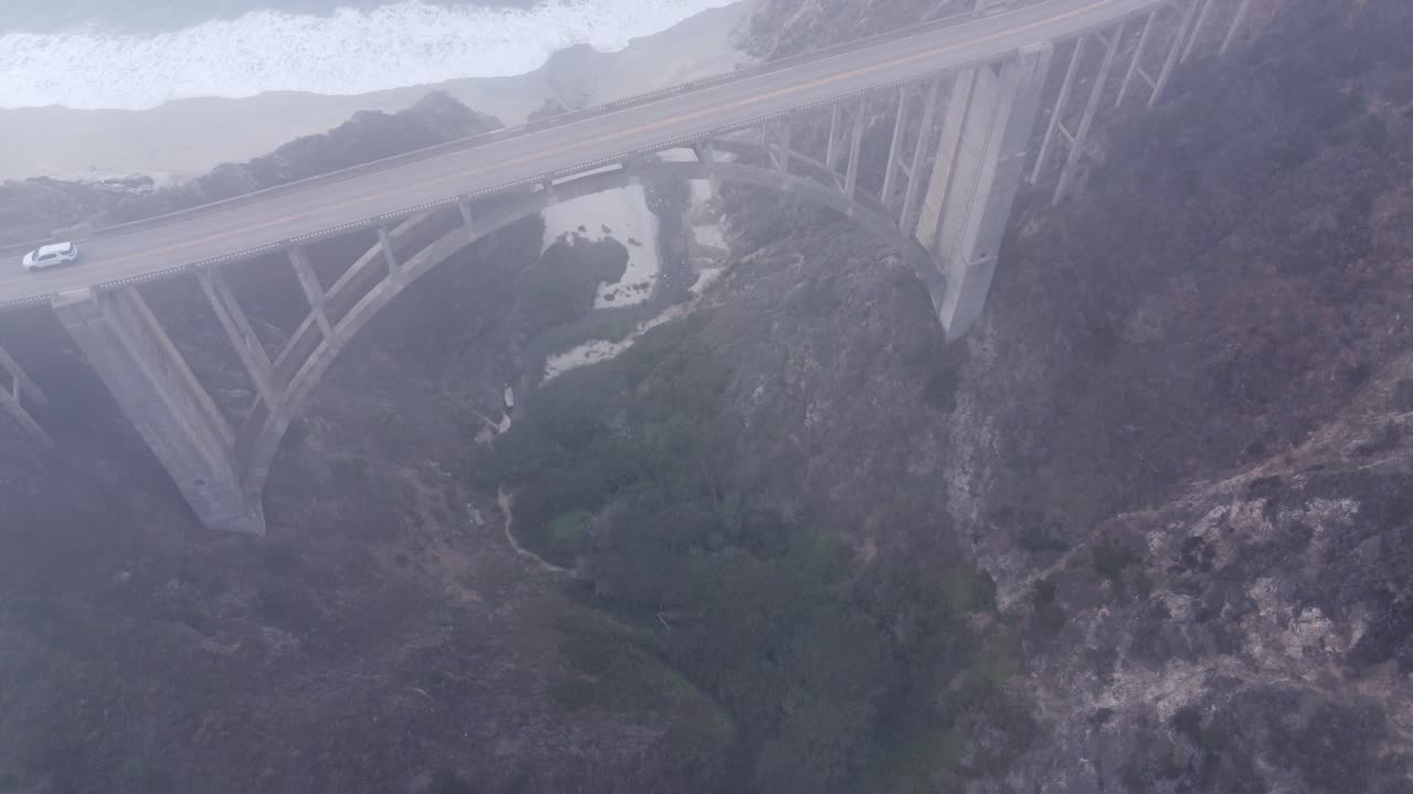 Drone shot of a foggy bridge next to the ocean.