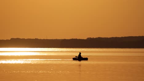 old fisherman in a boat on orange background of sunset. beautiful evening river and a man floating in a rowboat with fishing rods.