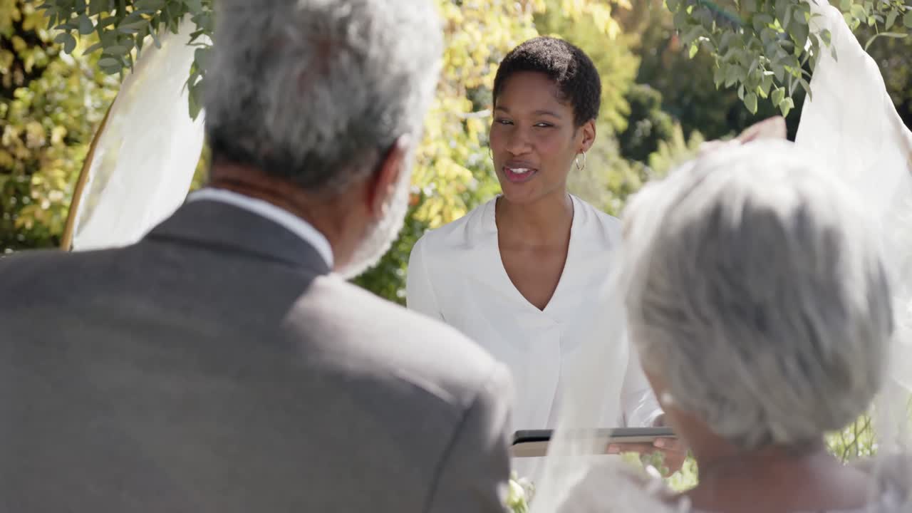 아프리카계 미국인 여성이 정원에서 두 인종의 부부의 결혼식을 치르고 있습니다.