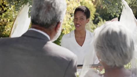Mujer-Afroamericana-Oficiando-Ceremonia-De-Boda-De-Una-Pareja-Birracial-Mayor-En-El-Jardín,-Cámara-Lenta