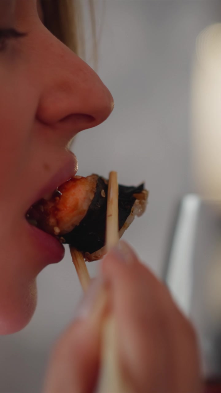 Close up of woman using chopsticks to eat sushi. scene focuses on action and texture details with soft lighting creating warm ambiance. Background remains blurred emphasizing intimate dining