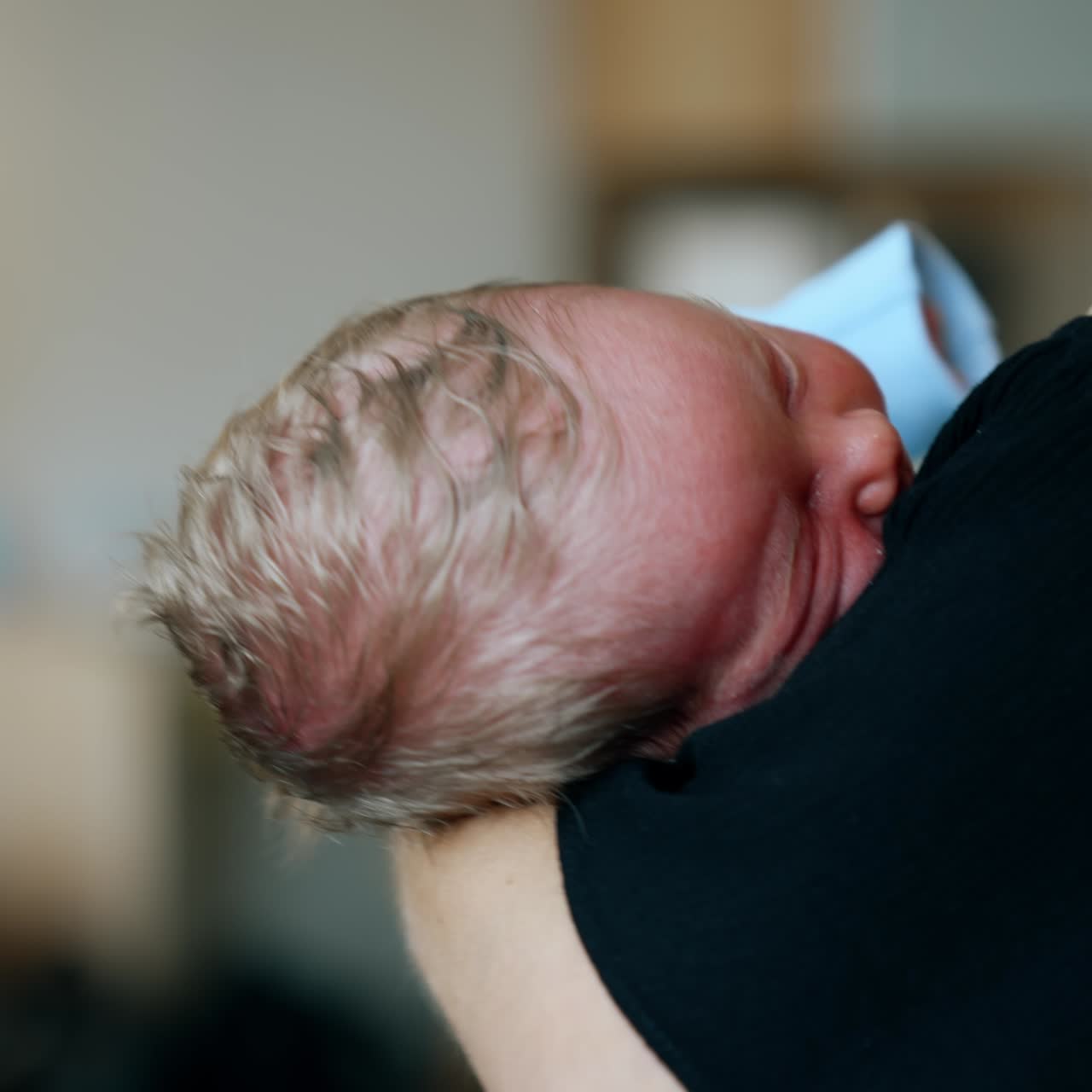 Blond head of a tiny sleeping newborn on mom's arm. Unrecognized mother waving her baby. Close up. Blurred backdrop