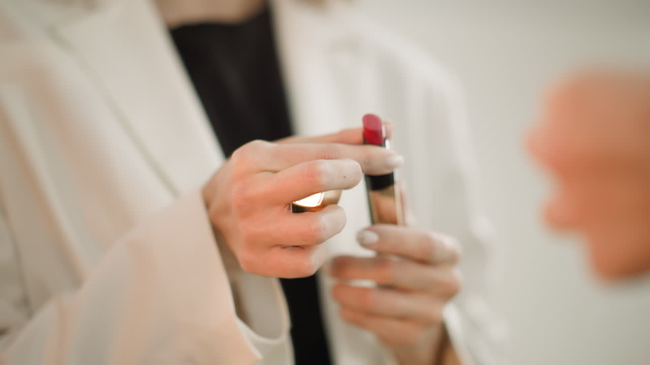 manos de una mujer girando un tubo de lápiz labial para pintar los labios de rojo
