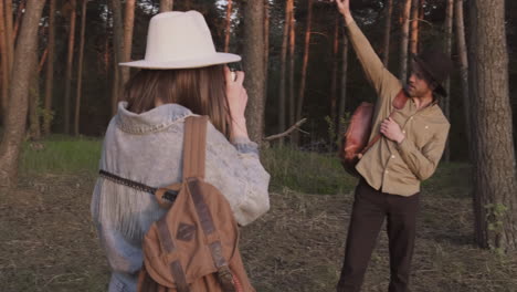 eine schöne junge frau fotografiert einen jungen mann mit hut im wald