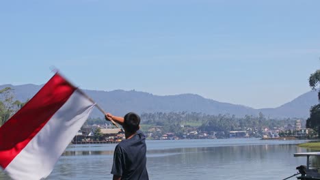 rear view of young man waving indonesian flag at lakeside. national pride in serene nature