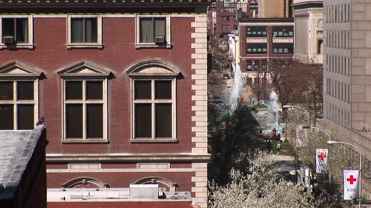 배경에 공원과 분수가 있는 브라운스톤 아파트 건물의 창문을 확대합니다.