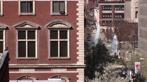 Acérquese-A-Una-Ventana-En-Un-Edificio-De-Apartamentos-De-Piedra-Rojiza-Con-Un-Parque-Y-Fuentes-Al-Fondo