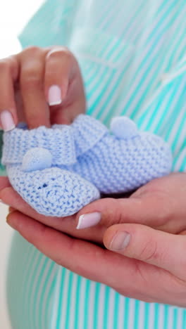 unrecognized pregnant lady holding tiny blue socks for future kid. male hand is supporting from below. close up. vertical video