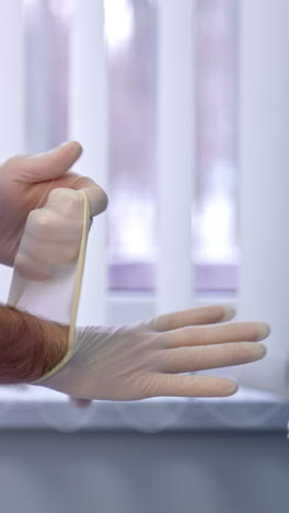 male medic wearing white coat putting on white latex gloves. close up. doctor's protection at hospital work. vertical video