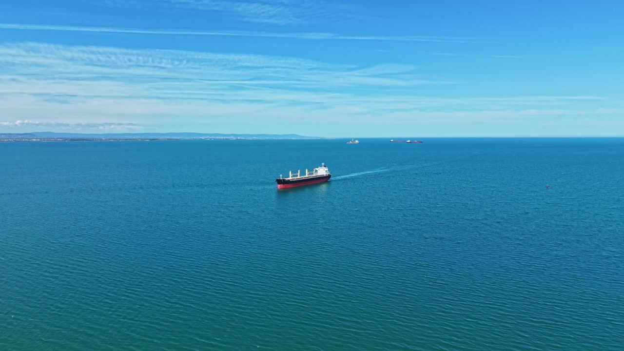 穏やかな海の風景。静かな青い海に一隻の貨物船が浮かび、遠くには広大な水平線が広がる。穏やかな空の下、一隻の貨物船が航行する静寂な海洋風景。
