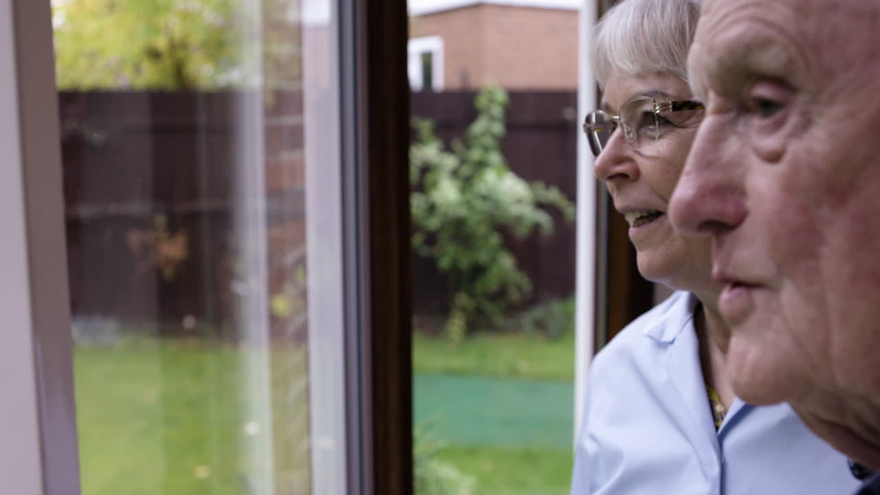 Elderly man looking out window at garden